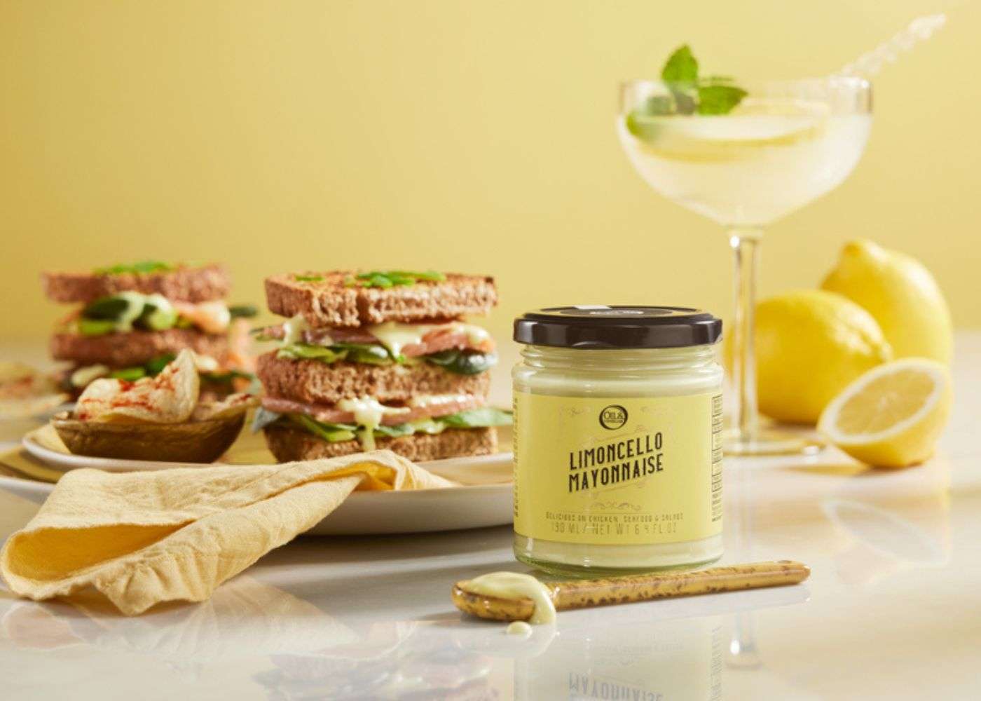 Jar of limoncello mayonnaise with a sandwich in the background. A gourmet condiment pairing for summer meals.