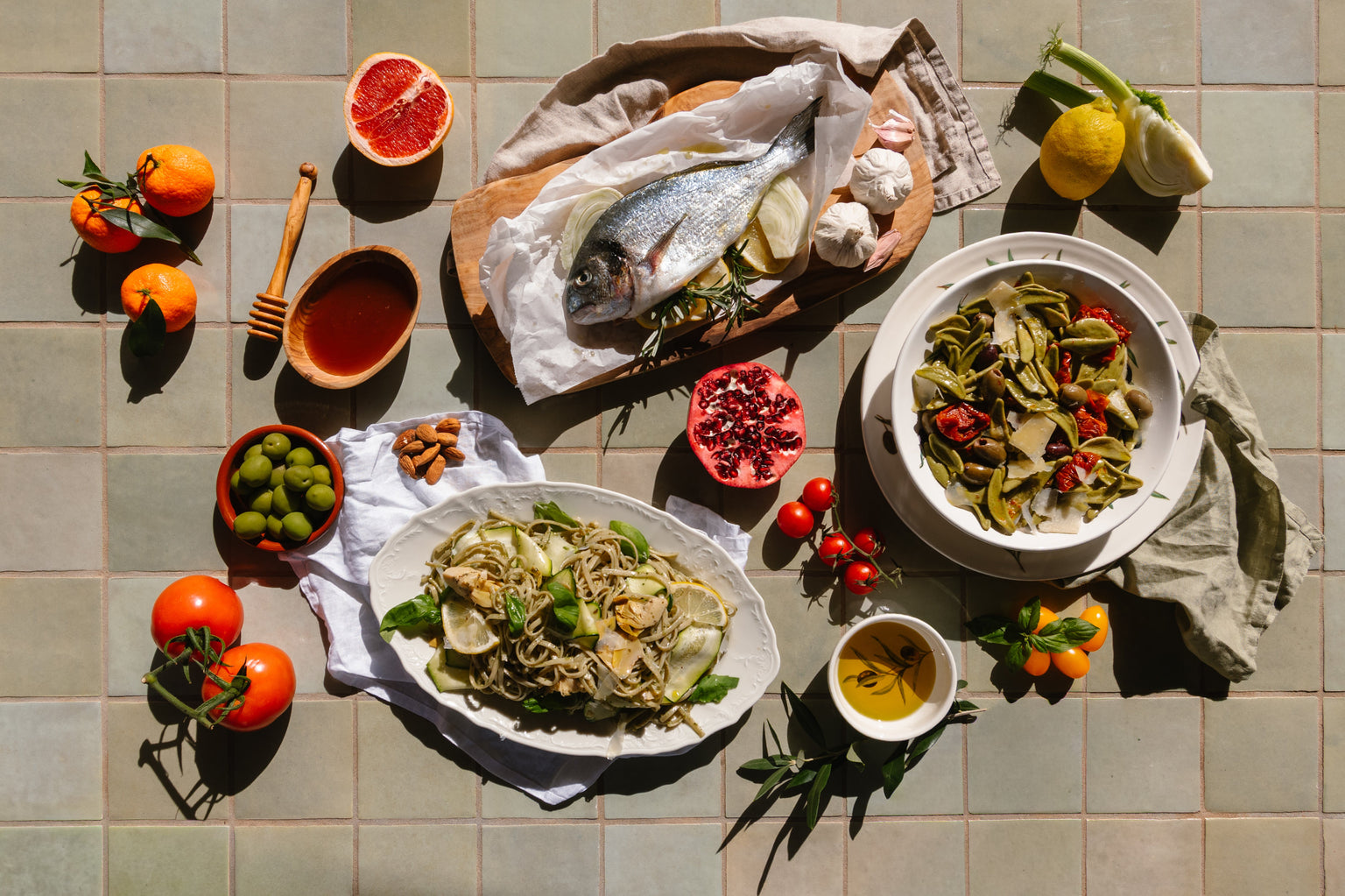 Table with various dishes of food including pasta, fish, and vegetables on a tiled surface.