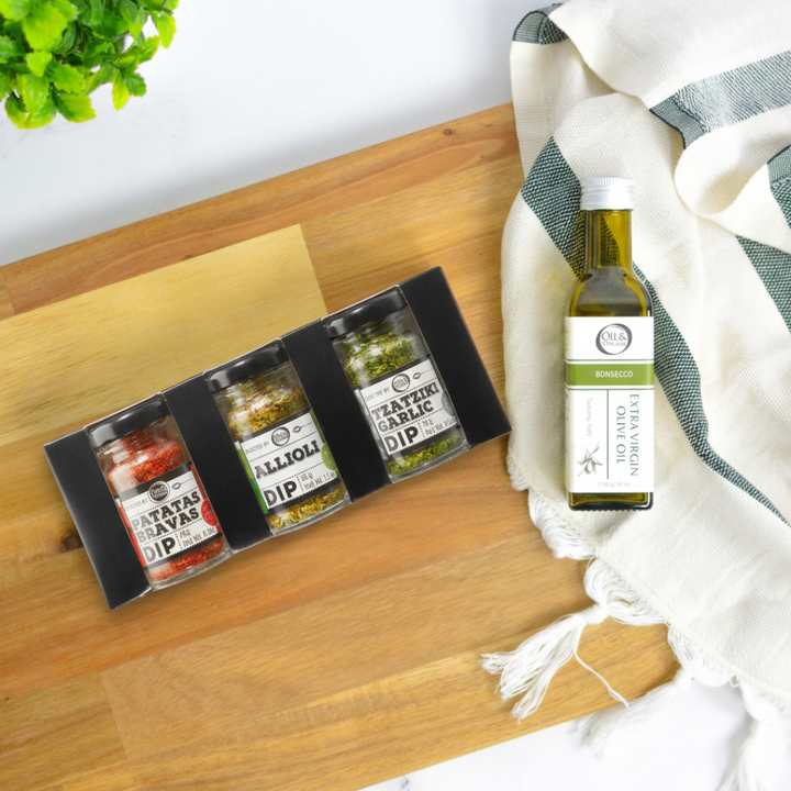 Set of Bruschetta seasoning jars and a bottle of olive oil on a wooden surface with a white tiled wall background.