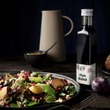 Plum Walnut vinegar bottle next to a salad plate with plums, pomegranates, and lettuce on a dark background