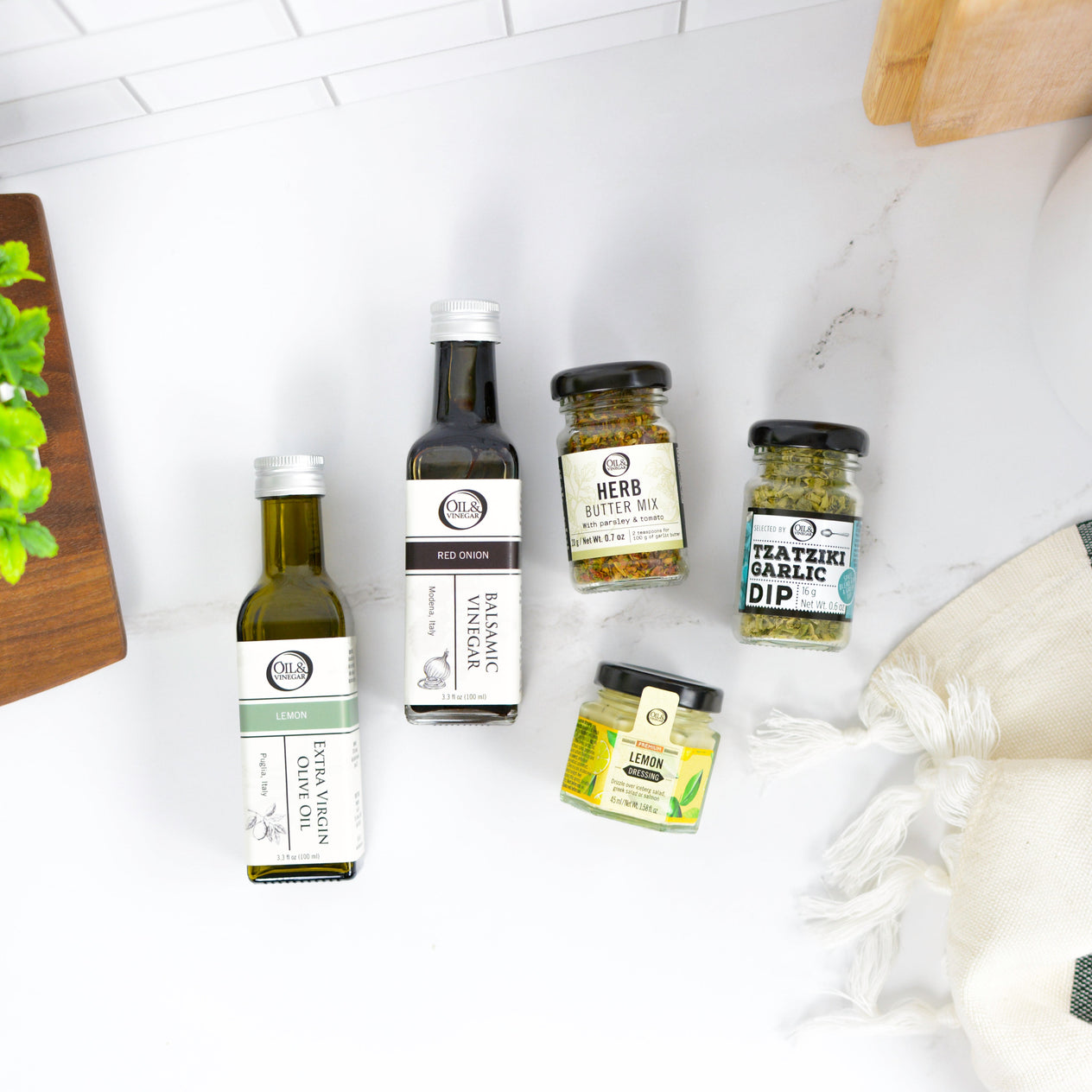 Collection of olive oil and balsamic vinegar bottles on a white surface with a wooden cutting board.