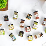 Assorted spice jars on a white surface with a plant and cup in the background
