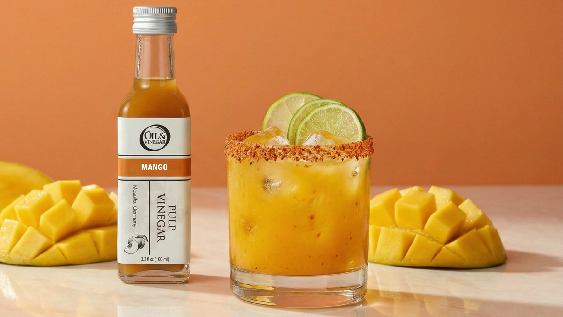 A bottle of Ols Mango Peel Vinegar stands next to a margarita glass filled with orange-yellow liquid, rimmed with red spice, and garnished with lime slices, with sliced mangoes on both sides against an orange background.