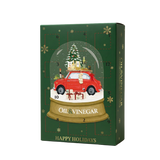 A Christmas advent calendar box with a dark green background, gold snowflakes, and a central illustration of a red car inside a snow globe with a Christmas tree and gifts. The box is labeled 'OIL & VINEGAR' and 'HAPPY HOLIDAYS'.