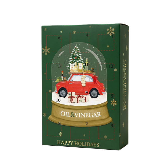 A Christmas advent calendar box with a dark green background, gold snowflakes, and a central illustration of a red car inside a snow globe with a Christmas tree and gifts. The box is labeled 'OIL & VINEGAR' and 'HAPPY HOLIDAYS'.