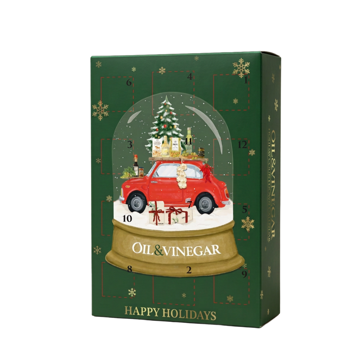A Christmas advent calendar box with a dark green background, gold snowflakes, and a central illustration of a red car inside a snow globe with a Christmas tree and gifts. The box is labeled 'OIL & VINEGAR' and 'HAPPY HOLIDAYS'.